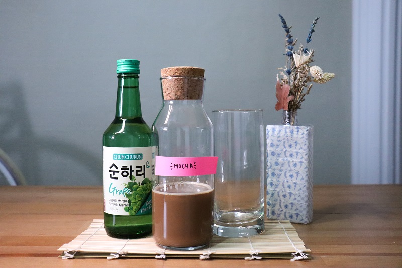 A bottle of grape soju, mocha and cocktail glasses displayed on a table.